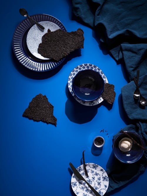 Une présentation artistique bleue avec des assiettes et bols indigo ou à motifs blanc et bleu accompagnées de couverts noirs placés au hasard.