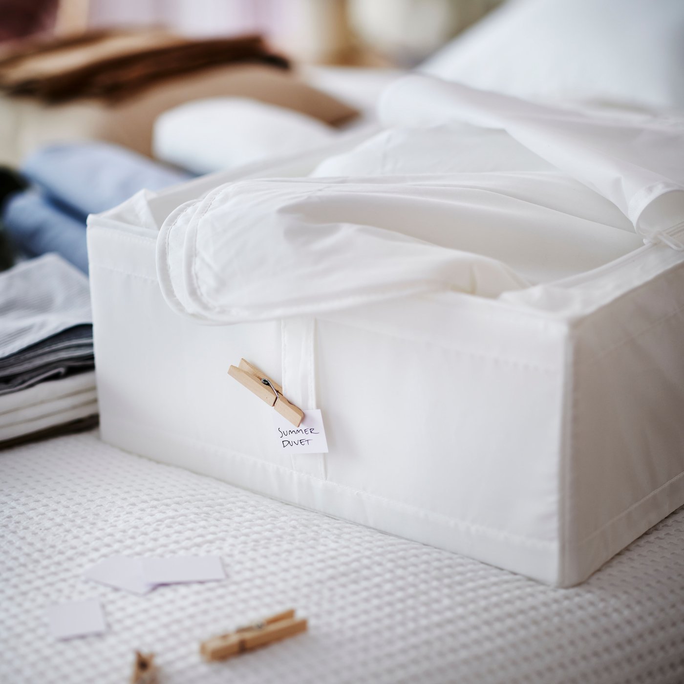 A white bed covered in a white VARELD bedspread with a white SKUBB storage box on top holding white bed textiles.