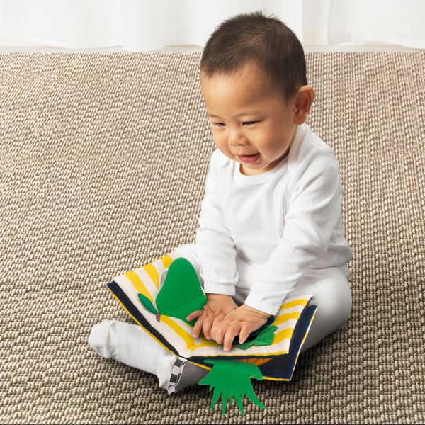 Child sat on a rug playing with the KLAPPA textile book