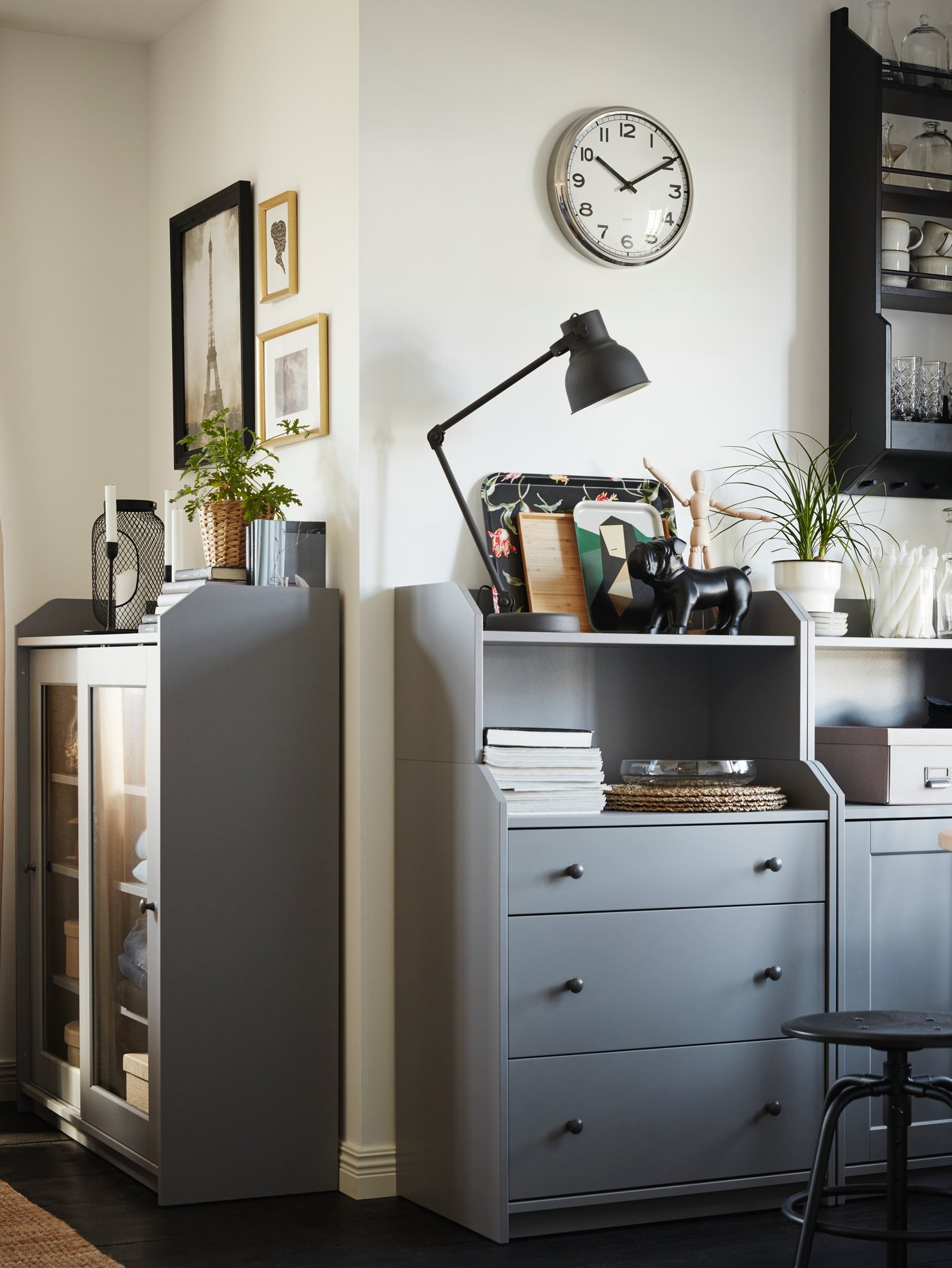 A cabinet, a glass door cabinet and a chest of drawers in grey, with shelves holding decorative items and a black lamp.