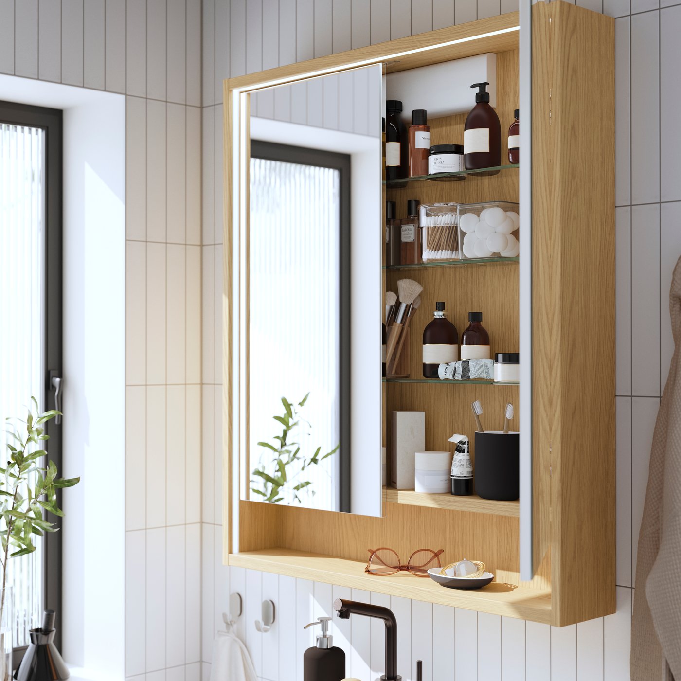 An oak effect FAXÄLVEN mirror cabinet with built-in lighting and two mirror doors has a door open, showing toiletries inside.