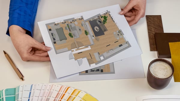 Projektantka wnętrz IKEA prezentująca kartki z wydrukiem rzutu z góry zaprojektowanego pomieszczenia. Obok na blacie leży wzornik kolorów i próbki materiałów.