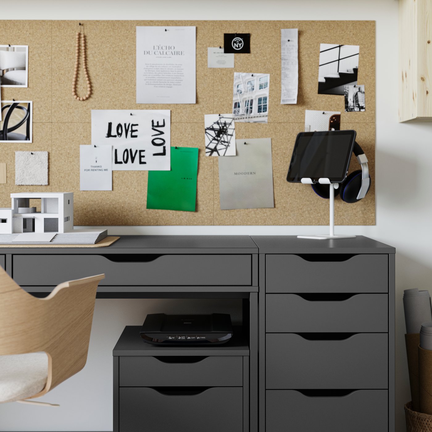 Et ALEX skrivebord og to skuffeelementer på hjul i mørkegrå-sort, med en opslagstavle i kork over og en konferencestol foran.