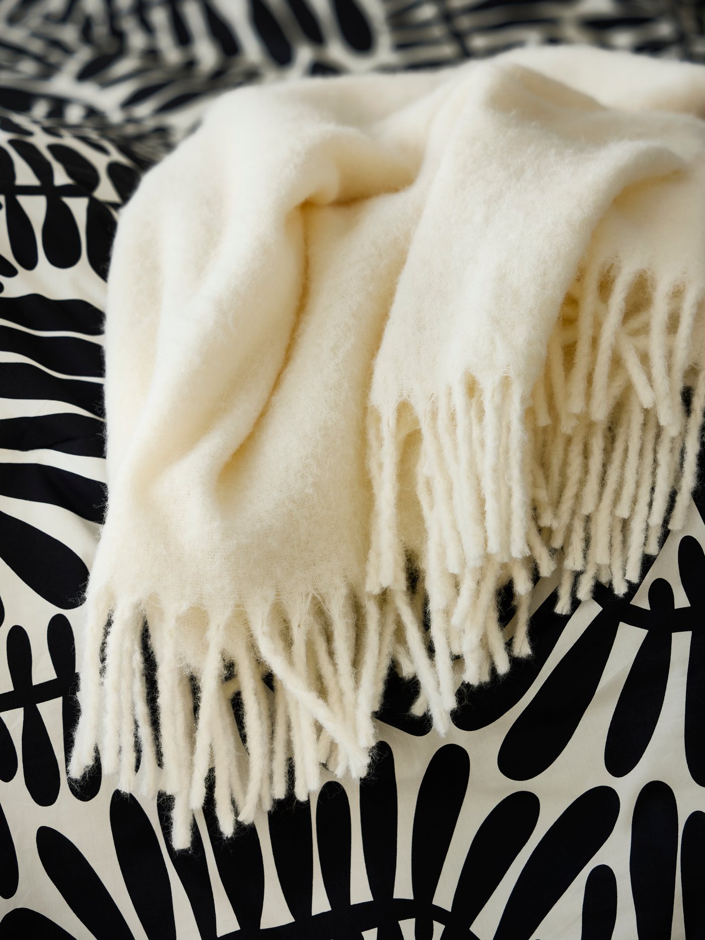 Close‑up van een offwhite KLIPPOXEL plaid boven op een zwart‑witte MAJSMOTT dekbed.