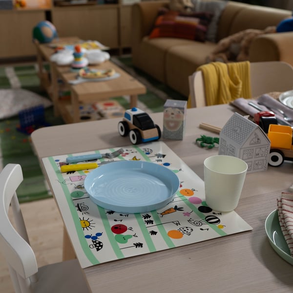 Un posto tavola per bambini con un piatto azzurro, una tovaglietta illustrata con disegni divertenti e un bicchiere, pronti per la pappa.