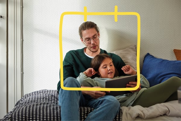 Een man en een kind zitten op de bank en kijken op een tablet.