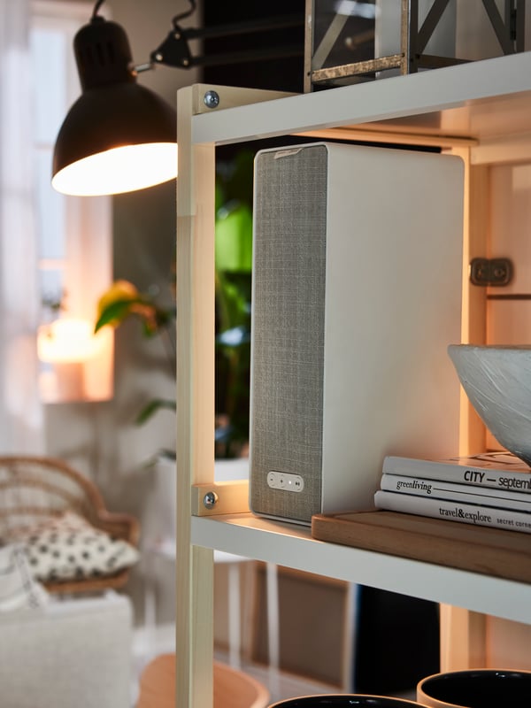 A hand holding up the IKEA Home smart app in front of a living room showing a screen with different options.