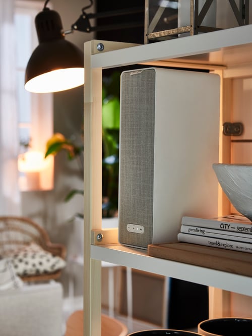 Side view of a SYMFONISK bookshelf speaker set on the shelf of an EKENABBEN open unit, and illuminated by a work lamp.