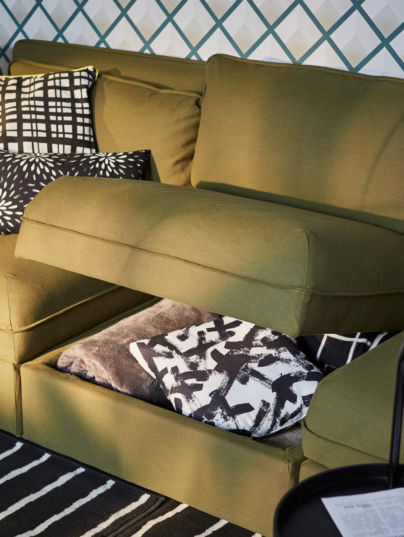 A VALLENTUNA green modular sofa unit with storage compartment propped open, black and white patterned pillows under.