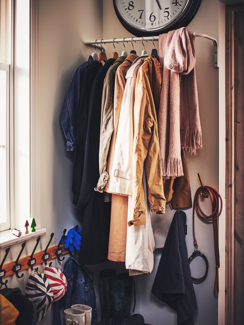 Hallway with a white clothes bar made of steel supporting multiple clothes next to a beige rack with 5 hooks.