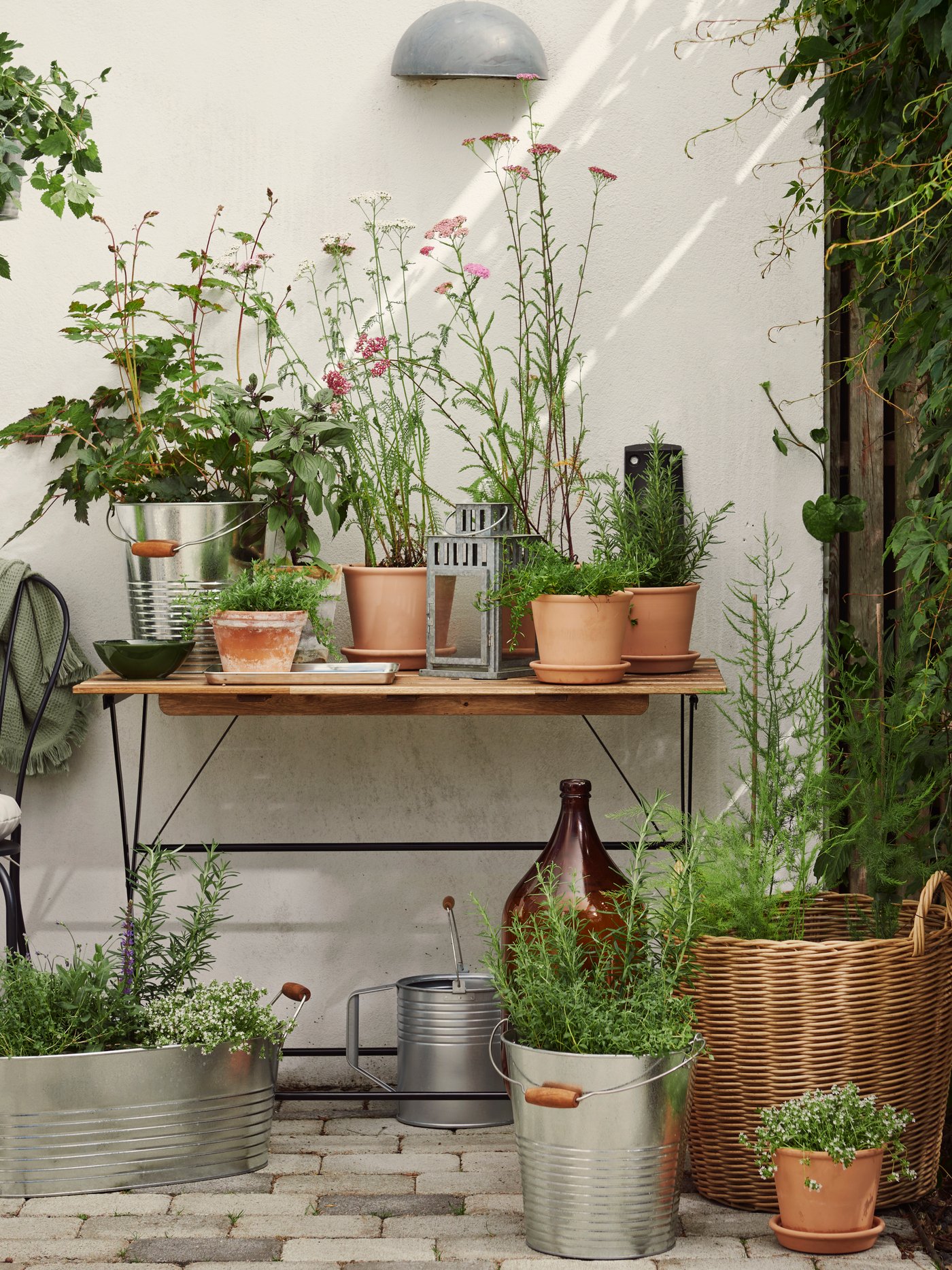 Un tavolo marrone chiaro di fronte a una parete esterna bianca, piena di piante verdi in vaso e fiori.