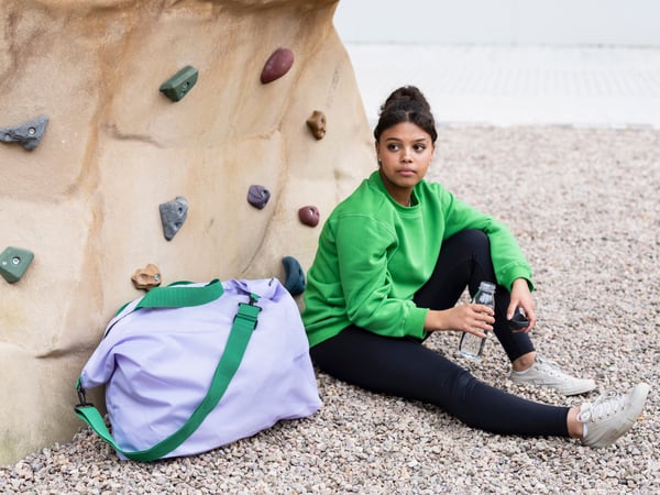 En kvinde sidder foran en klatrevæg med en lilla RÄCKLA taske