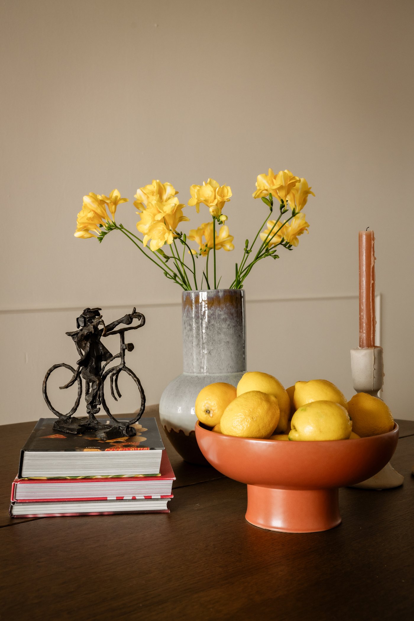 Close-up van een tafel, waarop verschillende items staan, waaronder bloemen in een grijze vaas en een roodbruine BLOMVECKLARE schaal. 