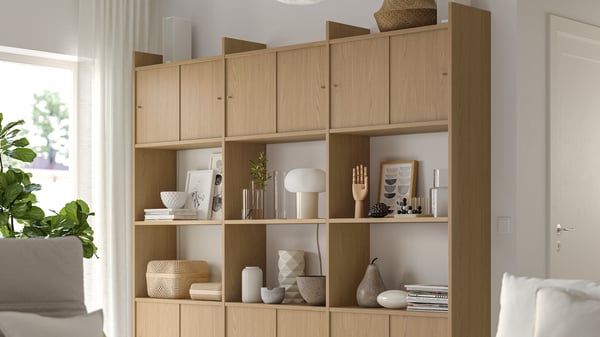 Wooden shelf with decor items, lit by natural light from a window. A plant and part of a white sofa are visible.