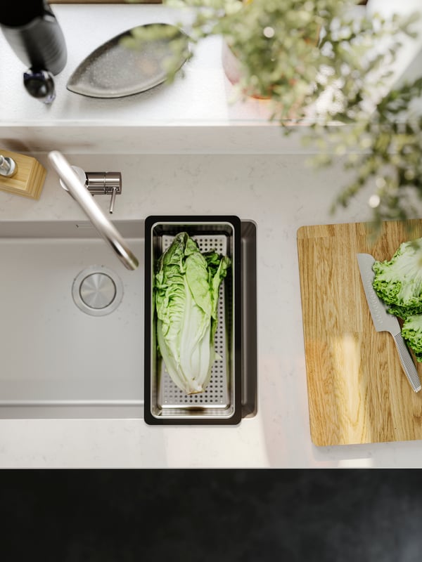 A stainless steel NORRSJÖN colander in the kitchen and a white worktop