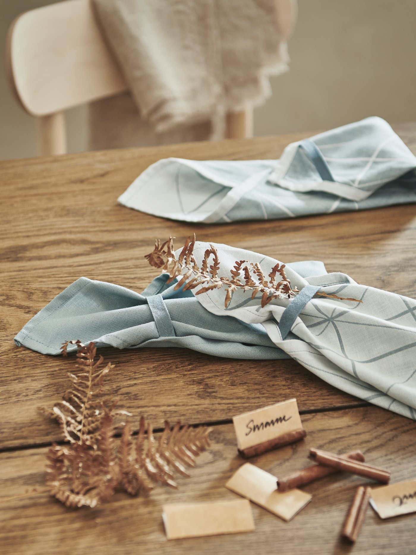 Tavolo in legno con decorazioni, segnaposti con nomi scritti a mano e strofinacci SANDVIVA azzurri piegati, che serviranno per una festa.