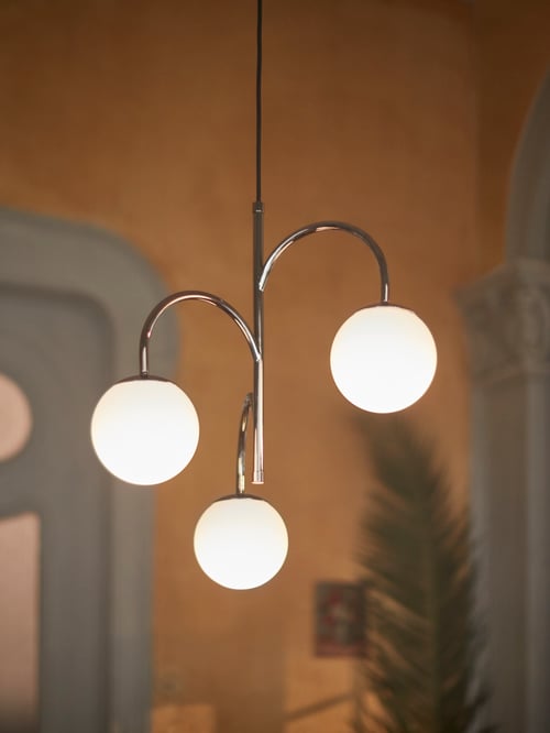 Living room with high ceiling, rustic paint, and chrome-plated metal pendant lamp with three frosted glass shades.