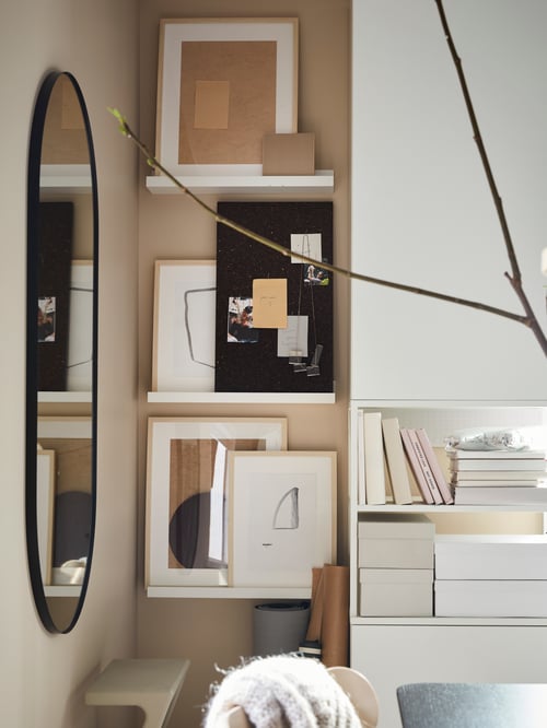 Wall-mounted picture ledges containing frames and a brown memo board with pins. On the adjacent wall is an oval mirror. 