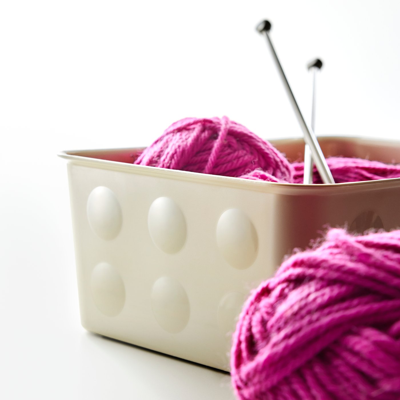 Nahaufnahme einer NOJIG Sortierbox, in der rosa Strickwolle und Stricknadeln aufbewahrt sind.