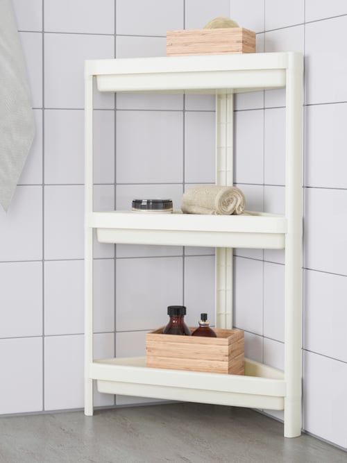 O baie cu plăci ceramice albe, etajeră de colț VESKEN cu prosoape și cutii de lemn amplasate pe polițele de sus și de jos.
