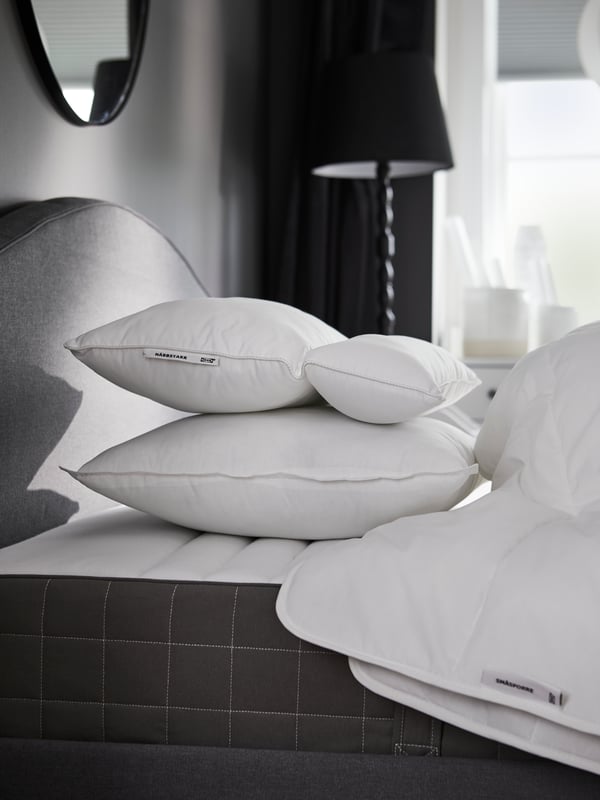 Een vrouw in grijze pyjama staat in een lichte kamer en houdt een KLUBBSPORRE ergonomisch kussen met meerdere standen in haar armen.