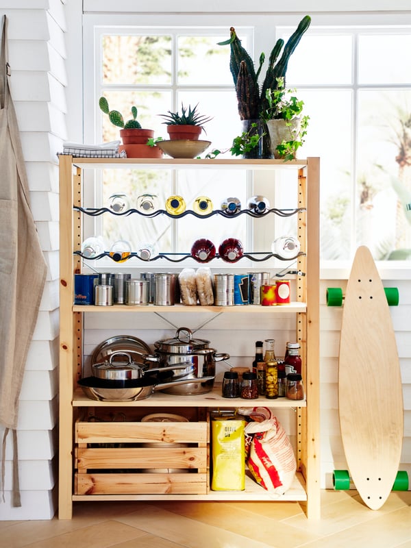 A wooden shelving unit with a bottle rack storing cookware, cans, jars and bottles, and a wooden box on the bottom shelf.