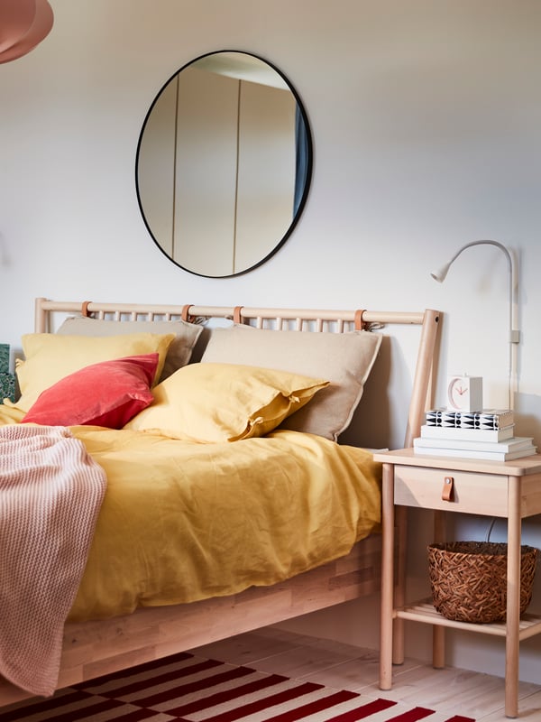 A BJÖRKSNÄS bedside table and bed with yellow PUDERVIVA bed linen and INGABRITTA throw, and a mirror on the wall behind.