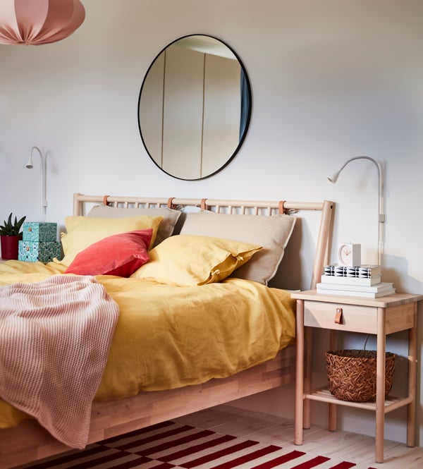 A BJÖRKSNÄS bedside table and bed with yellow PUDERVIVA bed linen and INGABRITTA throw, and a mirror on the wall behind.