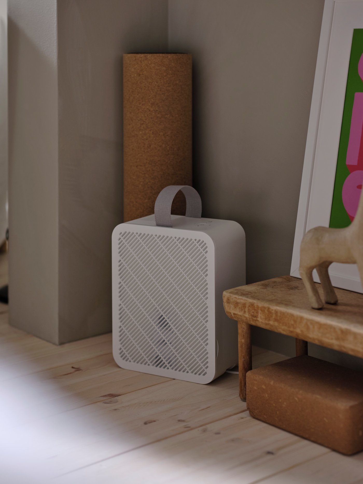 A white UPPÅTVIND air purifier on a light wood floor inside a grey alcove with a wooden horse and a bench on one side.