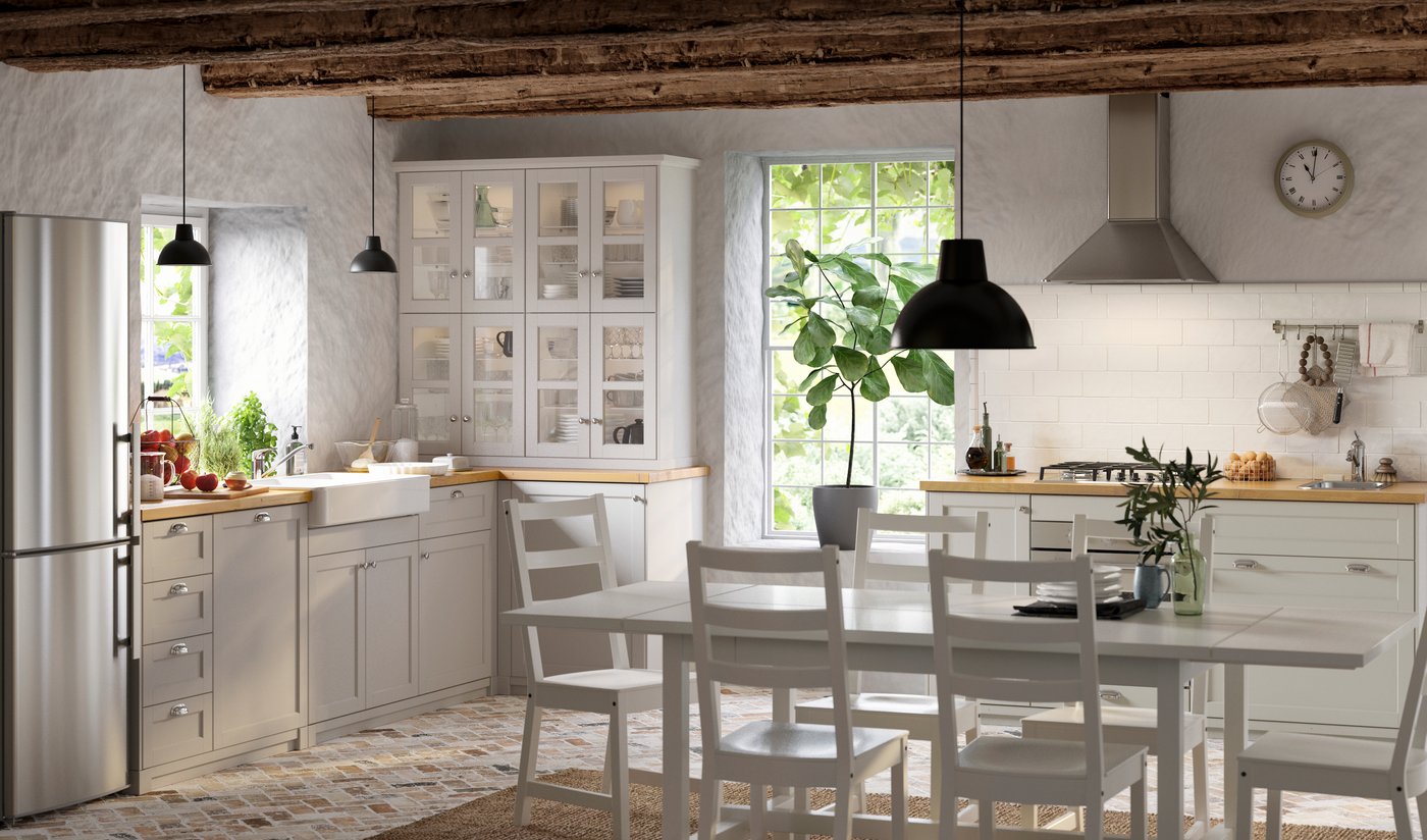 Et gråt LERHYTTAN køkken i et rustikt rum med grove, små fliser i jordnære farver på gulvet og fritlagte bjælker på væggen.