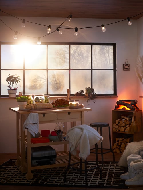 Wohnzimmer mit Servierwagen, Hockern, Lichterkette, Kamin, Essen, Behältern mit Deckeln, Koffer, Kleidung, Teppich.