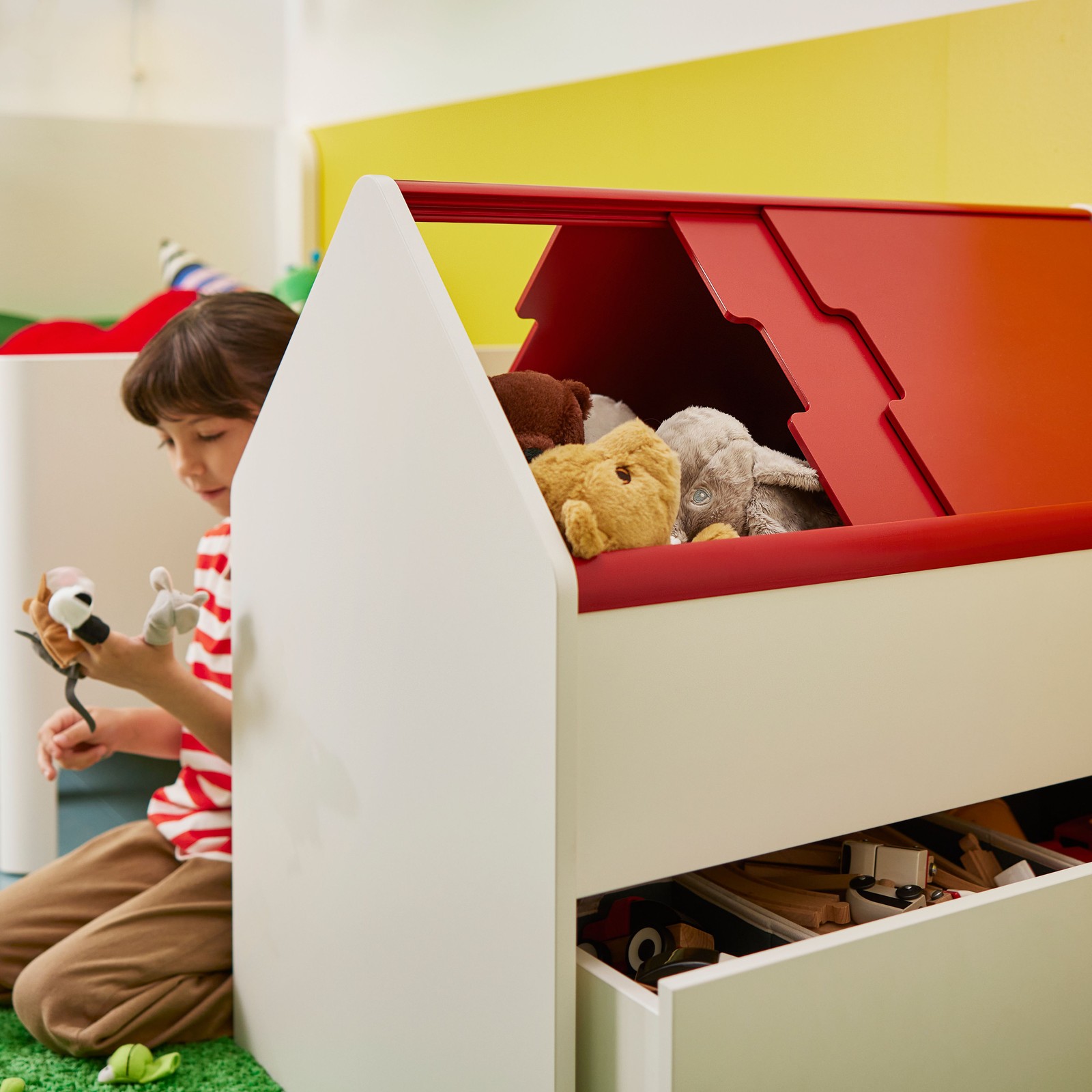 Devojčica se igra plišanim igračkama i sedi iza VITBJÖRN elementa za odlaganje s fiokom punom igračaka. Pozadi je BUSUNGE produživi krevet.