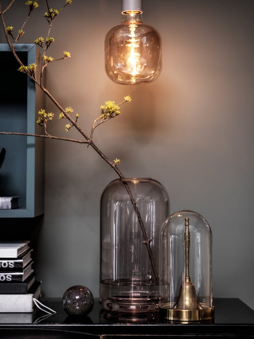 Le dessus d’un piano avec un dôme en verre BEGÅVNING, une brindille dans un vase en verre et d’autres objets décoratifs.