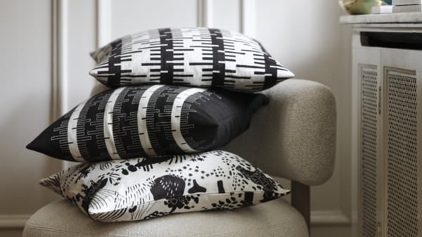 A stack of cushions in different patterns and in black, white and grey tones, placed on a armchair.