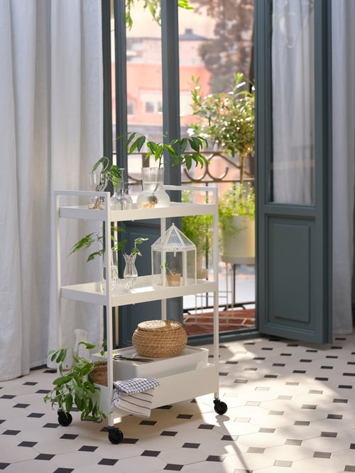 バルコニーのドアの近くにあるNISSAFORS/ニッサフォース ワゴンに収納されたSESAMFRÖN/セサムフローン プラントスプレー、PÅDRAG/ポードラグ 花瓶、STÄRKT/ステルクト ミニ温室。