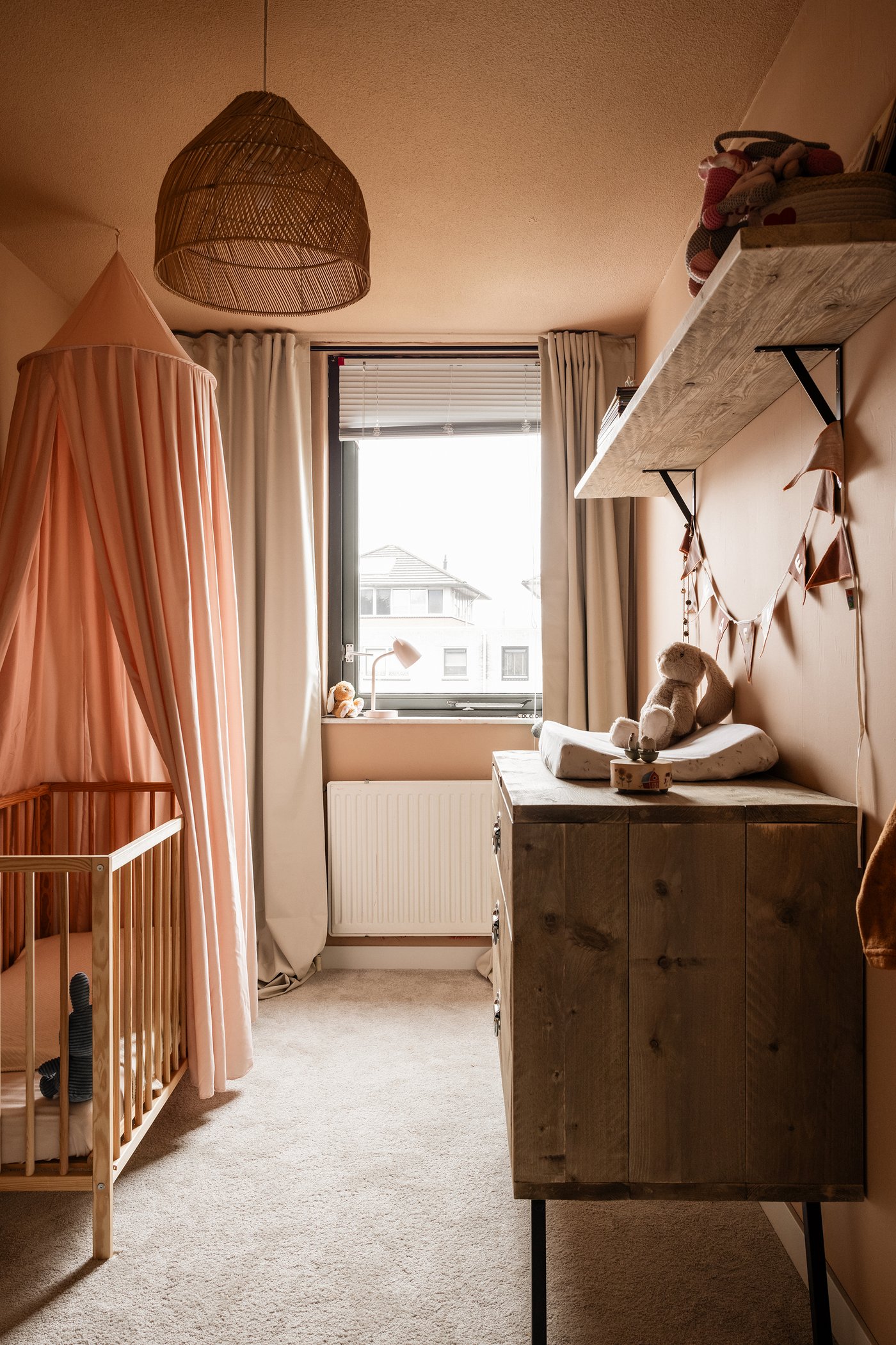 Kinderkamer met links een SNIGLAR babybedje, waarboven een klamboe hangt. Rechts staat een houten ladekast met daarop een verschoonkussen.