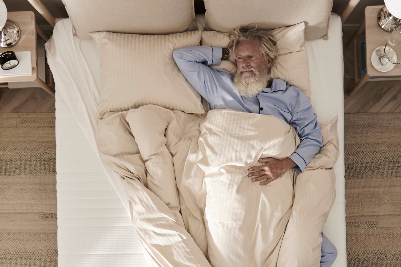 A birds eye view of a man laying on a white mattress with a light beige NATTJASMIN duvet cover.