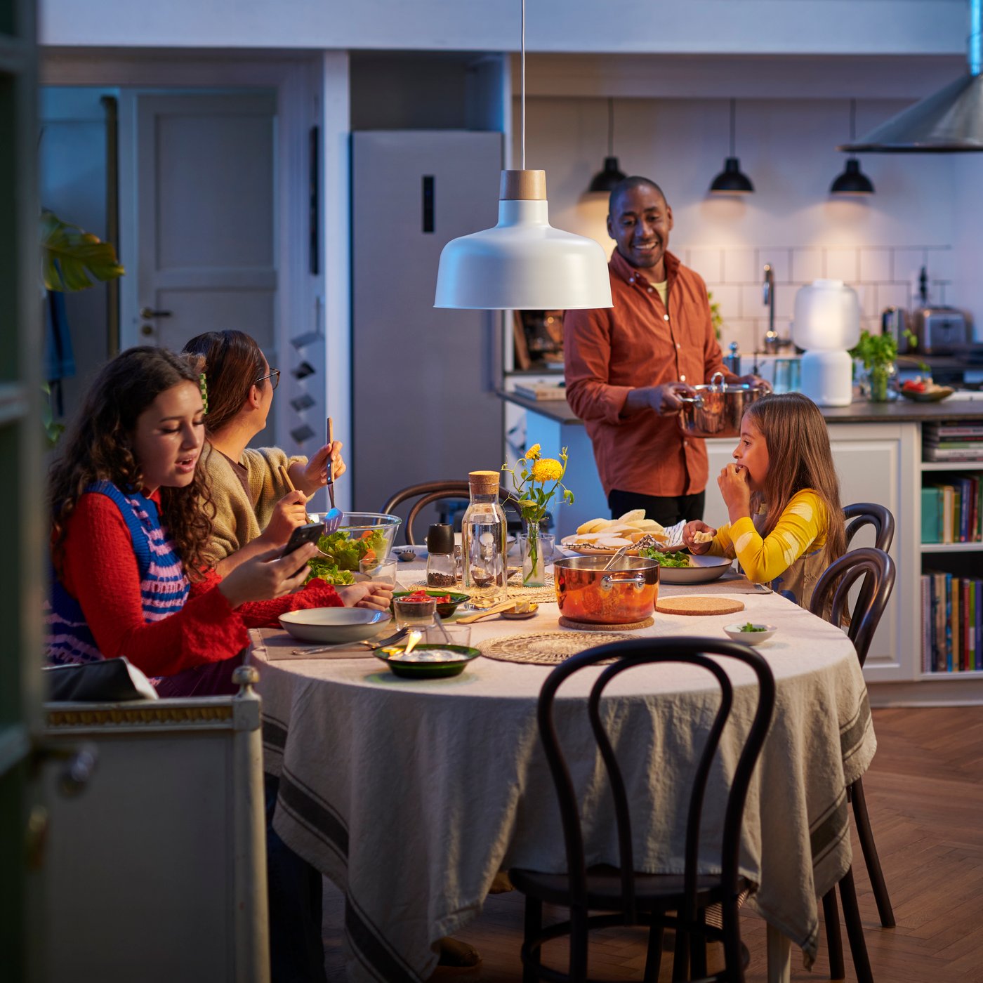 Eine Familie, die um den Esstisch sitzt, mit einem weissen/smart STARKVIND Luftreiniger im Hintergrund.