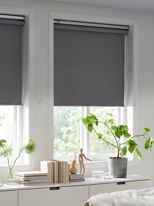 A bedroom with two FYRTUR block-out roller blinds, half-way down, in two windows above some chests of drawers.