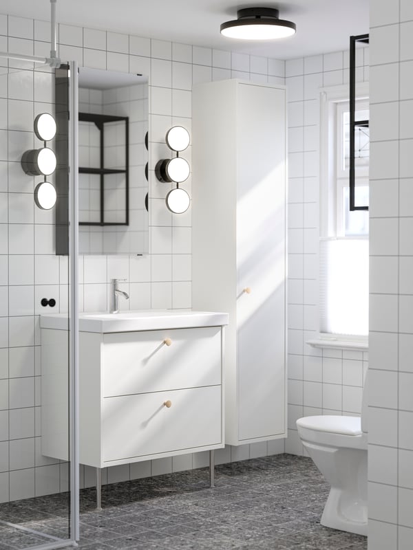 A bathroom with white tiles has two black KABOMBA LED wall lamps and a LETTAN mirror above a white HAVBÄCK wash-stand.