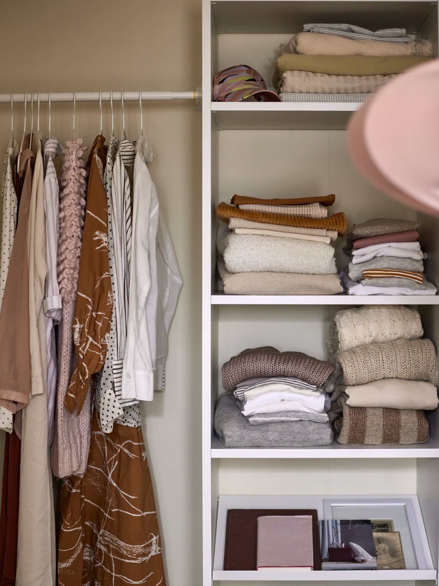 An organized AURDAL closet with shirts hanging on one side and sweaters on the shelves next to it.