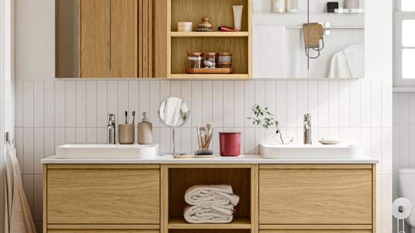 A white-tiled bathroom has ÄNGSJÖN bathroom furniture in oak effect, including a vanity with drawers and wall cabinets.