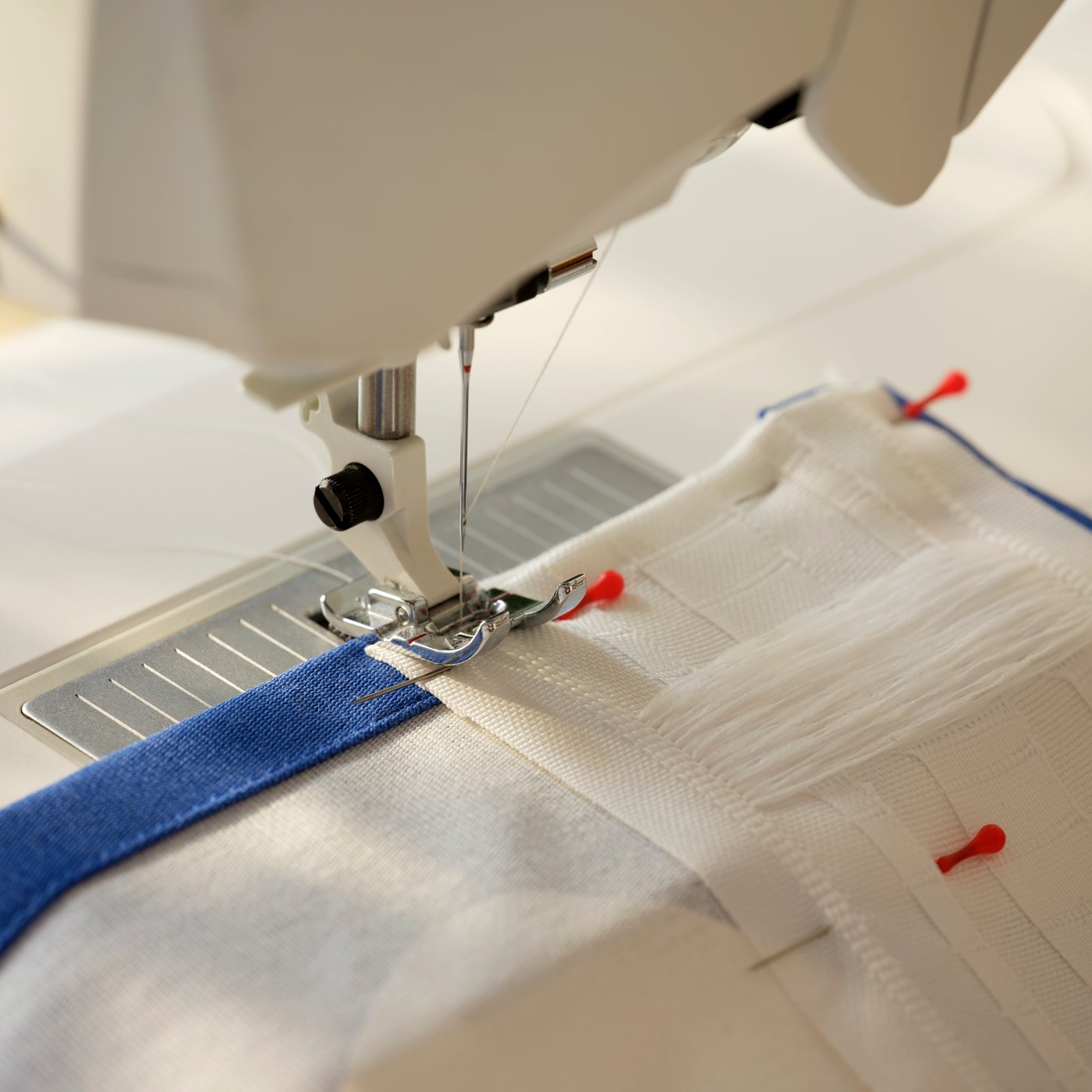 Symaskin som håller på att sy fållen på ett par gardiner. 