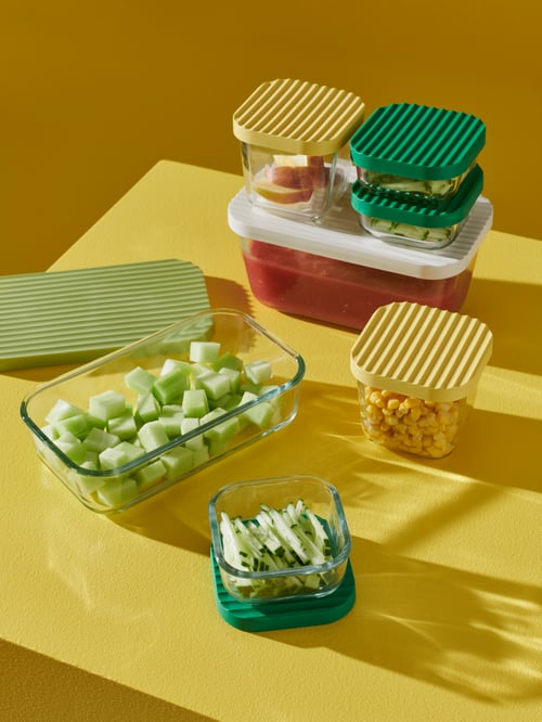 O fotografie aeriană a unui set de containere pentru picioare HAVSTOBIS cu produse alimentare pe o suprafață galbenă. Fiecare capac are o culoare diferită.