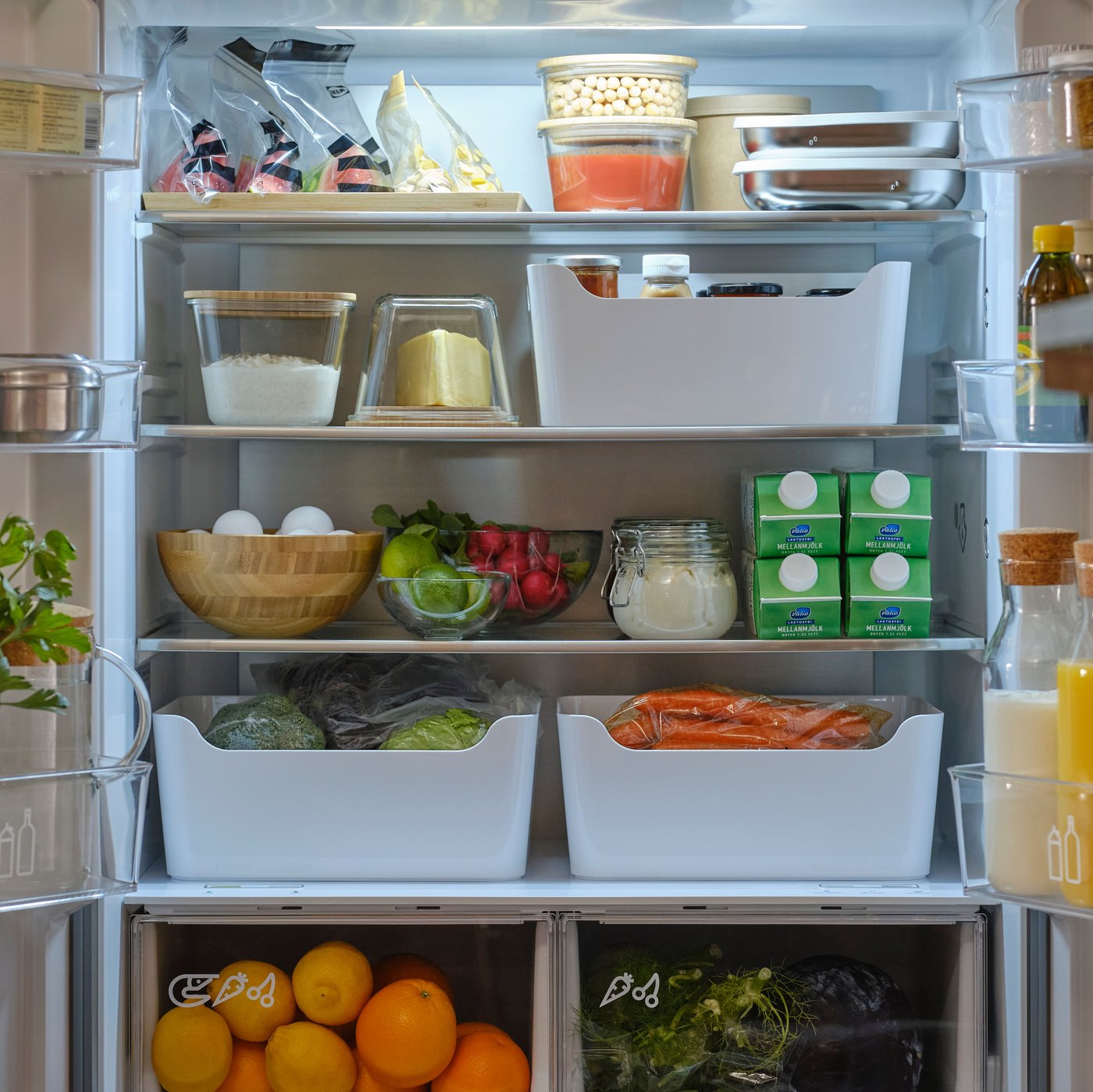 Ett kylskåp fyllt med diverse livsmedel, inklusive grönsaker, juicekartonger, salladsskålar, ägg och behållare med torrvaror.