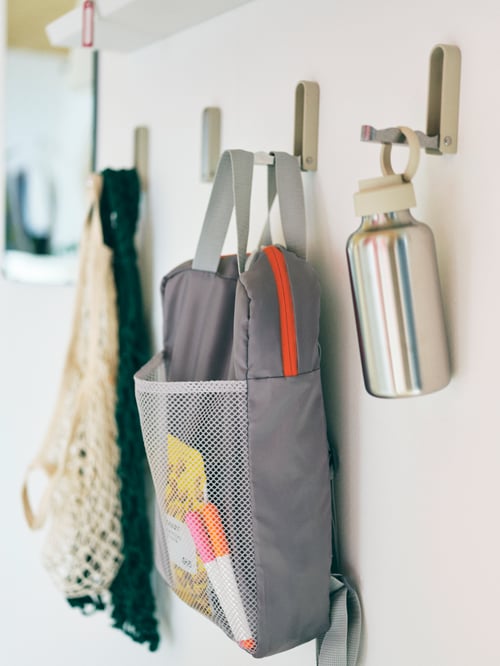 Drei KLYKET klappbare Haken an einer Wand. Daran sind u. a. ein PIVRING Rucksack, KUNGSFORS Einkaufsnetze und eine ENKELSPÅRIG Wasserflasche befestigt.