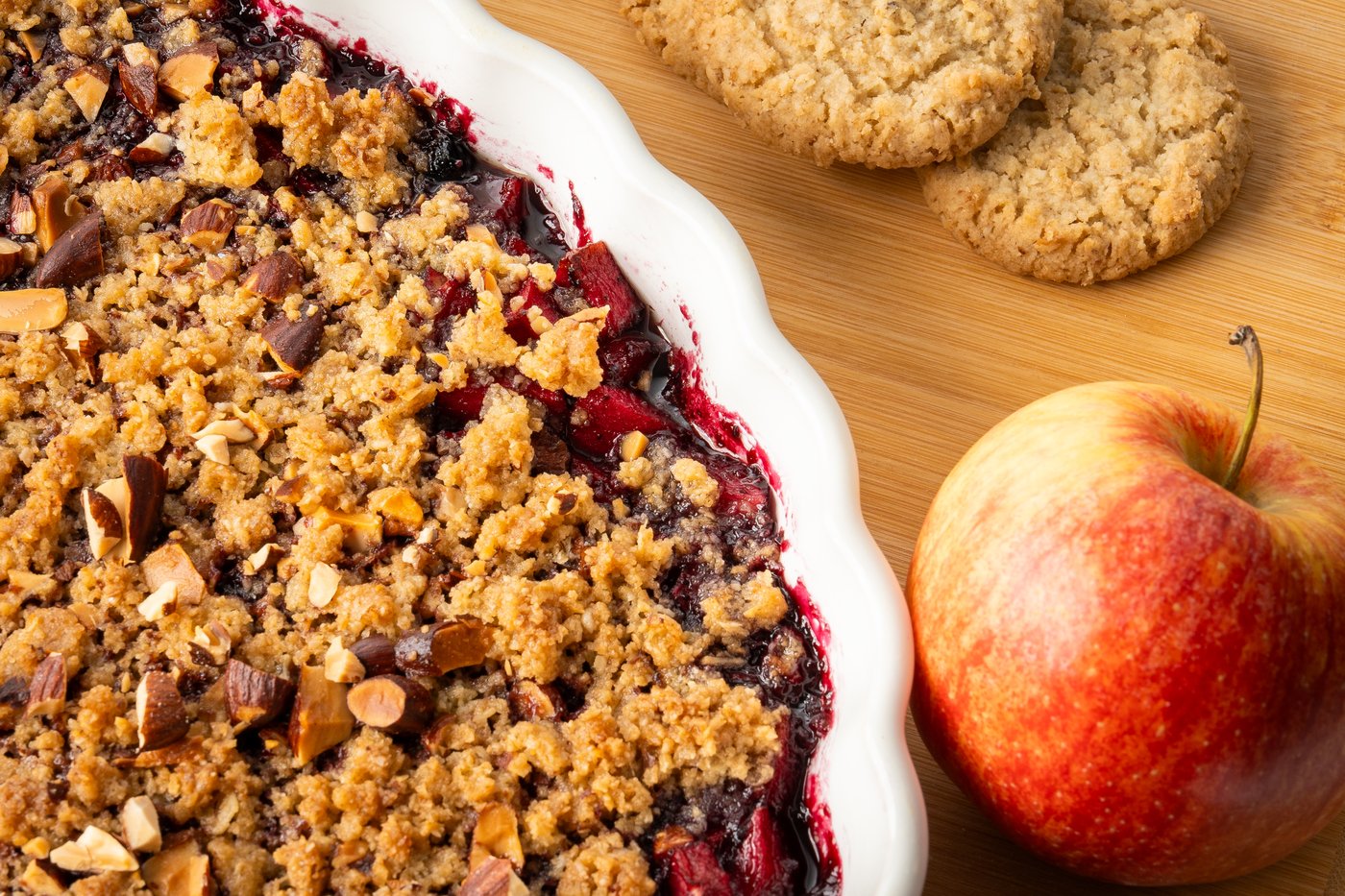 Nahaufnahme vom Apfel-Blaubeer Crumble in einer Auflaufform auf einem Schneidebrett präsentiert.