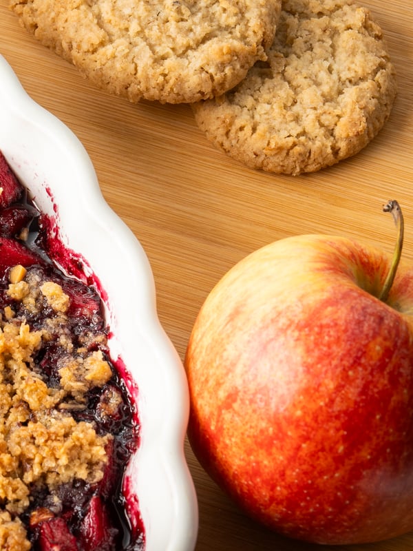 Nahaufnahme vom Apfel-Blaubeer Crumble in einer Auflaufform auf einem Schneidebrett präsentiert.