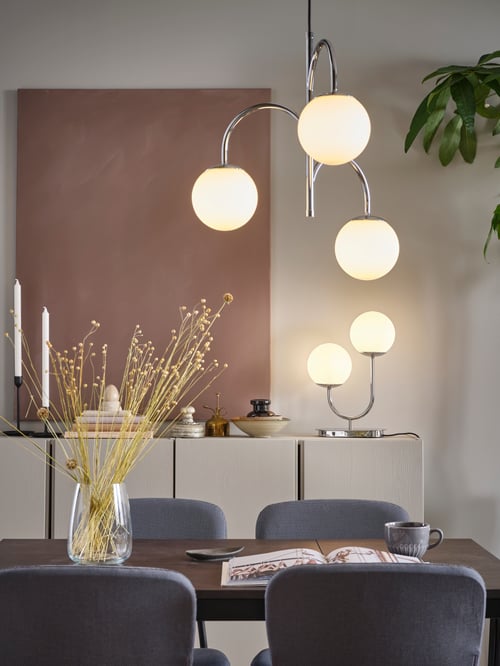 Dining room focus of a grey 3 armed pendant lamp made of steel, placed above a black extendable table and multiple chairs.
