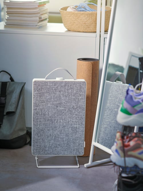 A FÖRNUFTIG air purifier sits on the floor next to a mirror, a yoga mat. A shelvin gunit with books and baskets sits behind.